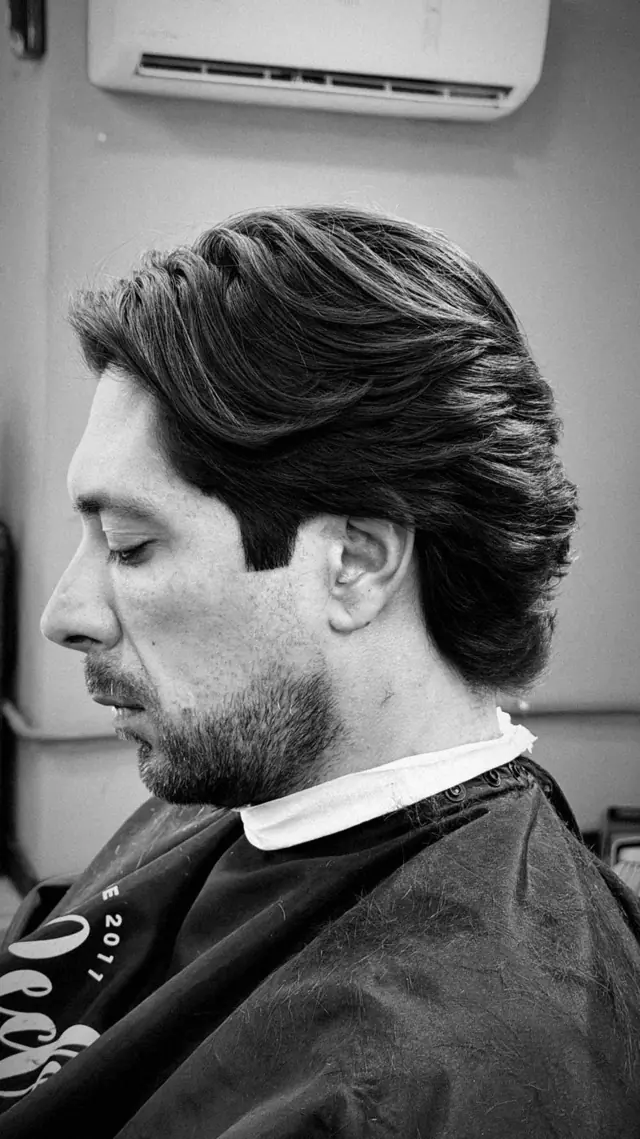 Cliente de perfil com corte finalizado e capa da barbearia
